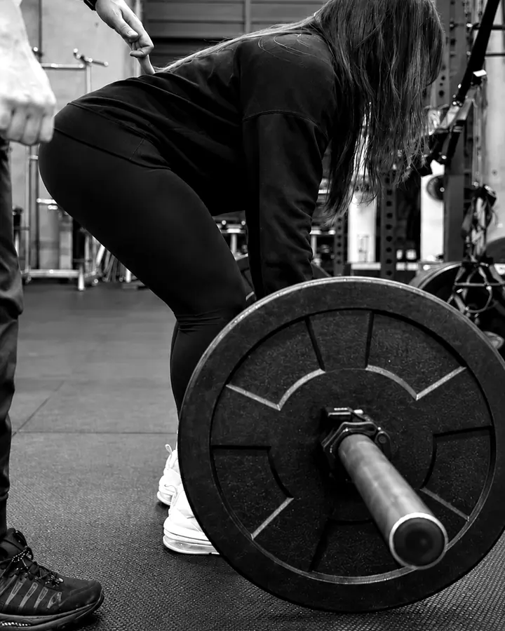 Client deadlifting a loaded barbell with Shayan cueing her hip hinge